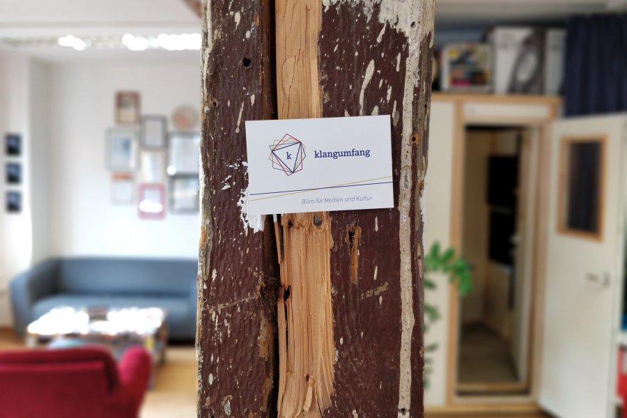 An einem Holzpfeiler mitten im Büro hängt eine Visitenkarte mit dem klangumfang-Logo.